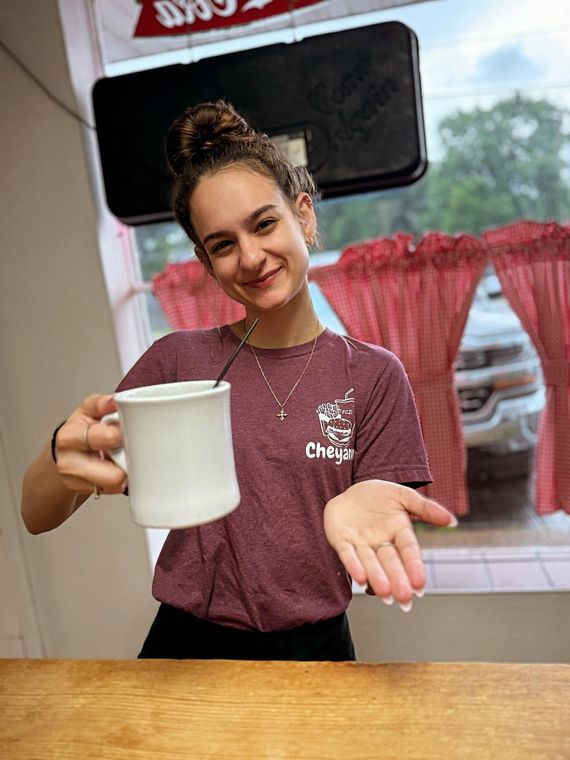 A server pours coffee into a white diner mug by the window