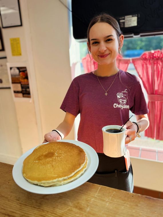 A server holds a giant pancake that covers the plate, with a coffee pot